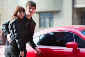 Two teenagers in front of red car